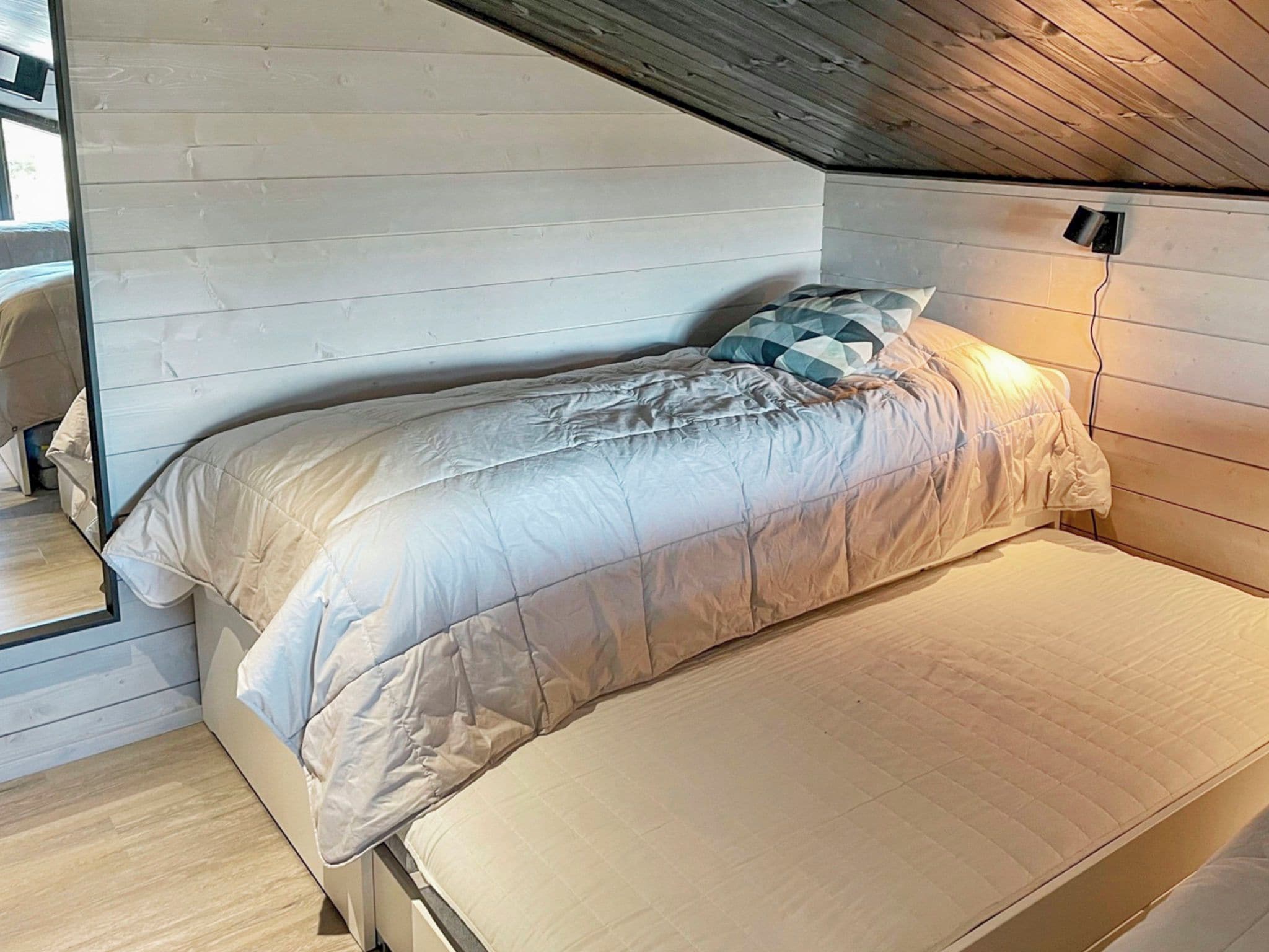 Ein Einzelbett mit gesteppter Matratze in einem Zimmer mit Holzwänden und schräger Decke.