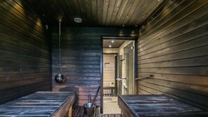 Sala de sauna com bancos de madeira, luminária pendente e porta visível para outro cômodo.
