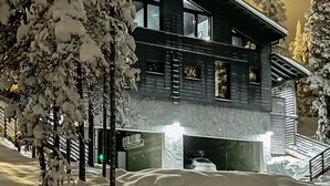 Um edifício moderno de dois andares com fachada escura e grandes janelas. Árvores cobertas de neve circundam o local.