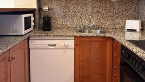 Cocina compacta con armarios de madera, lavavajillas, microondas, cafetera, lavaplatos y tostadora.