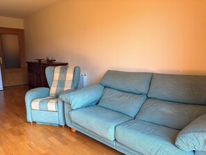 A living room with a sofa and armchair, wooden floor, and a cabinet.