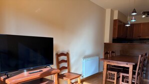 Un salón con televisor, muebles de madera, un radiador y una zona de cocina.