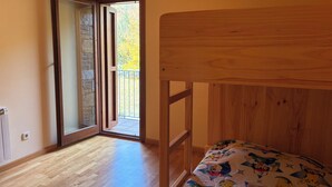 Una habitación con una cama litera de madera, una puerta corrediza de vidrio que da a un balcón exterior y un radiador en la pared.