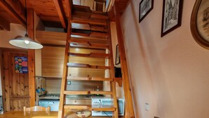 Eine Holztreppe führt zu einem Küchenbereich mit Esstisch und Stühlen, einem Fernseher und gerahmten Bildern an der Wand.