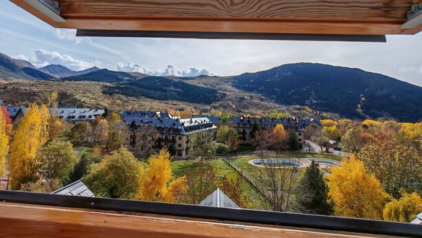 Blick aus einem Fenster auf ein Tal mit herbstlich gefärbten Bäumen, einen Pool und ein Gebirge.