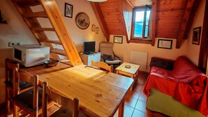 Ein gemütliches Blockhaus mit Holzvertäfelung, einem Esstisch, Stühlen, einem roten Sofa, einem Fernseher und einem Fenster mit Aussicht.