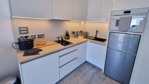 A modern kitchen with white cabinets, a black stove, a stainless steel refrigerator, and a wooden countertop.