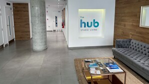 A modern hotel lobby with a large pillar, a sofa, a glass coffee table with magazines, and a sign reading "The Hub Studio Living".
