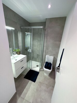 A modern bathroom with a glass-enclosed shower, a white sink with a plant, and a toilet with a towel. - Top Floor Studio-The Hub-Self Catering (Gibraltar)