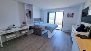 A modern bedroom with a bed, a desk, and a computer. There is a window with a view of the outdoors.