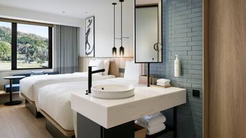 A modern hotel room with a large bed, a round sink, a mirror, and a view of a forest through large windows.
