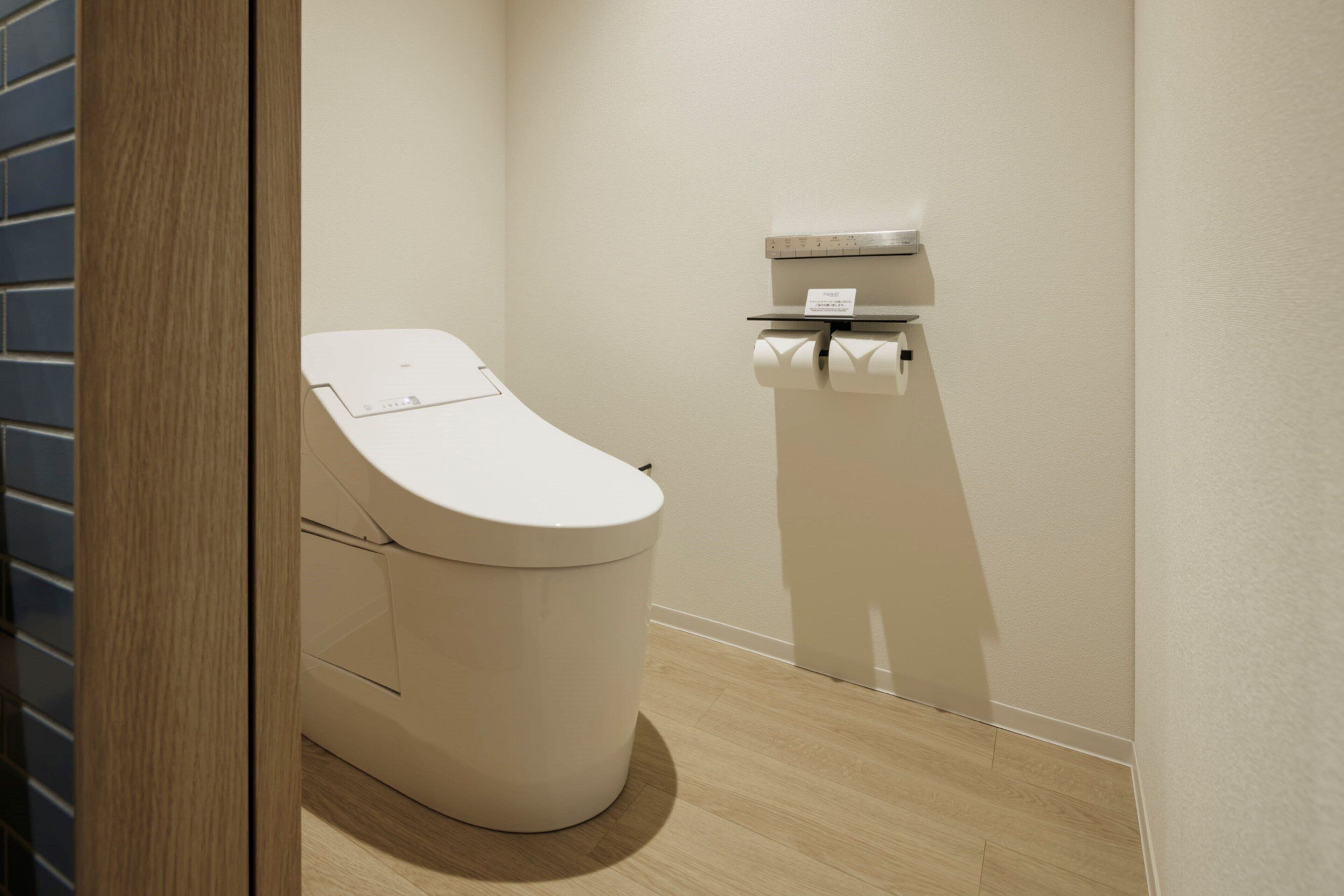A modern bathroom with a toilet, a paper towel dispenser, and a wooden floor.