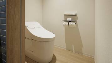 A modern bathroom with a toilet, a paper towel dispenser, and a wooden floor.