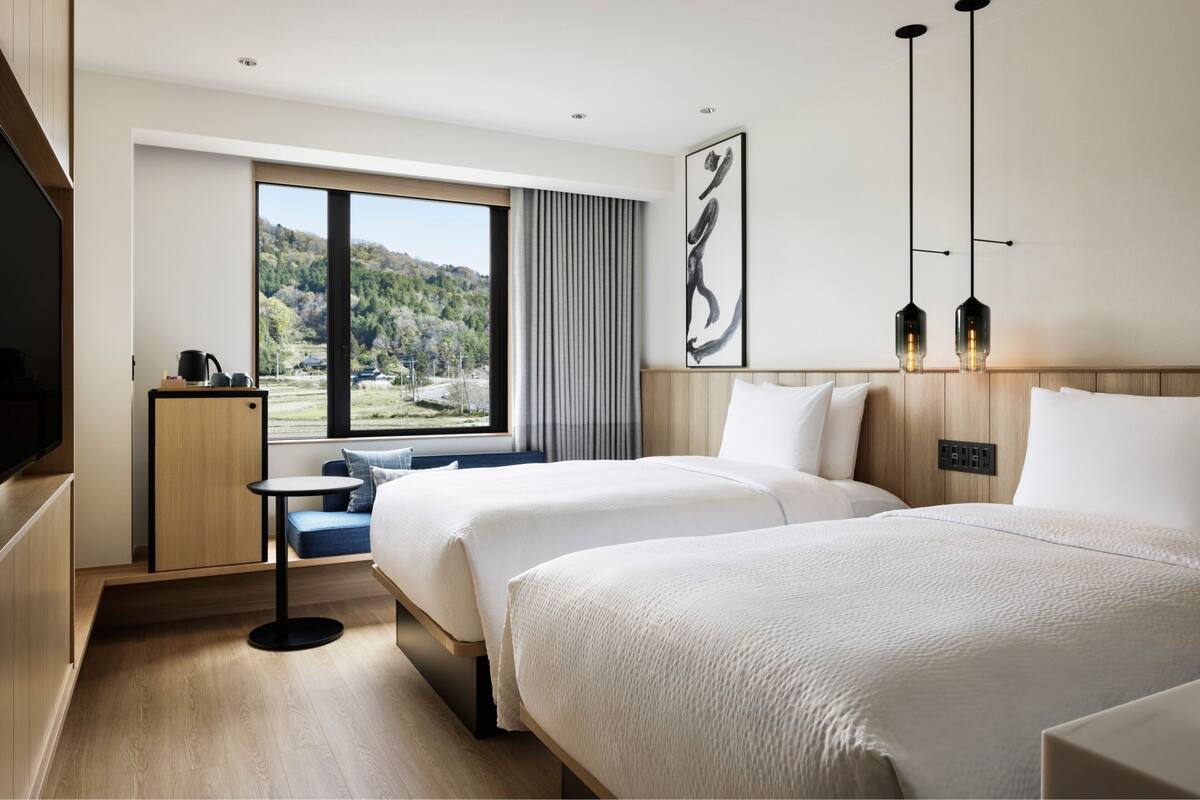 Ein modernes Hotelzimmer mit zwei Betten, einem kleinen Tisch, einem Fernseher und einem großen Fenster mit schöner Aussicht.