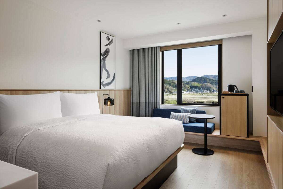 Ein modernes Hotelzimmer mit einem großen Bett, einer Sitzecke mit Blick und einem Fernseher.
