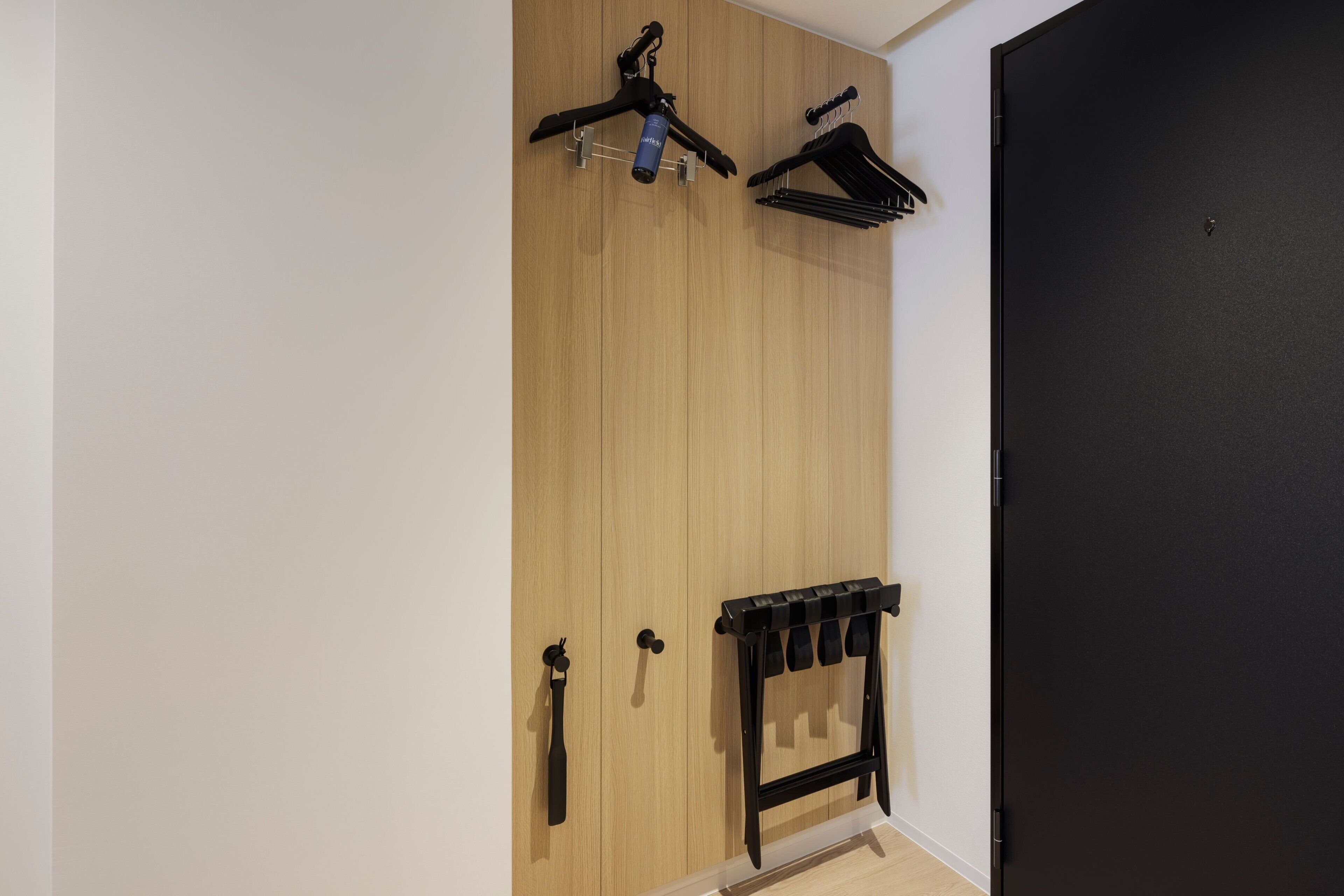 A room with a wooden wardrobe, a black door, and a black coat rack with hangers.