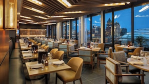 A modern restaurant with a long counter, individual booths, and large windows offering a city view. - The Trade, Autograph Collection (Milwaukee)