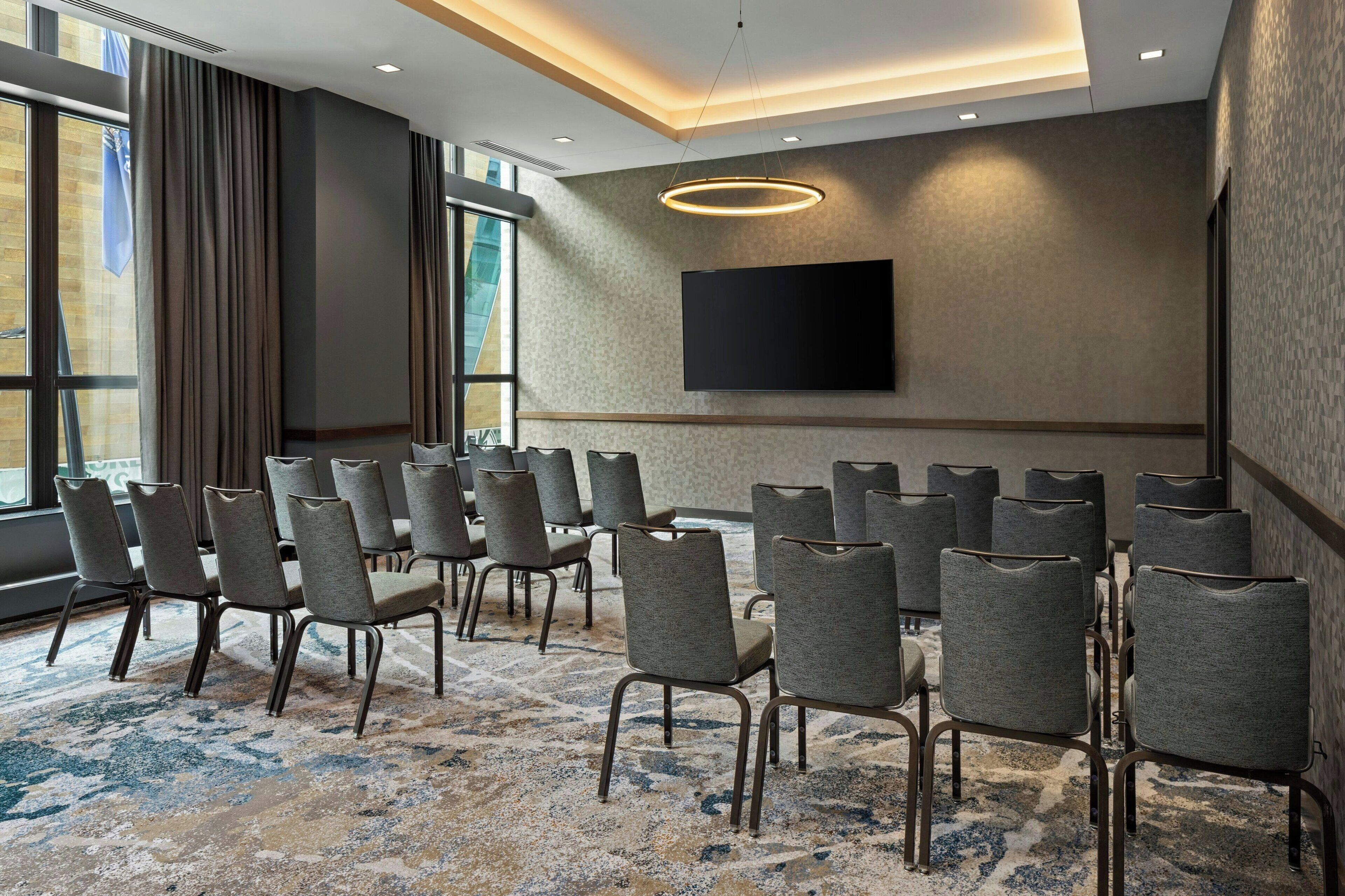 A conference room with rows of chairs, a large flat-screen TV, and a patterned carpet.