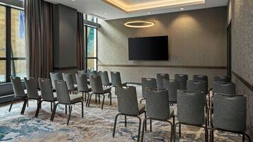 A conference room with rows of chairs, a large flat-screen TV, and a patterned carpet.