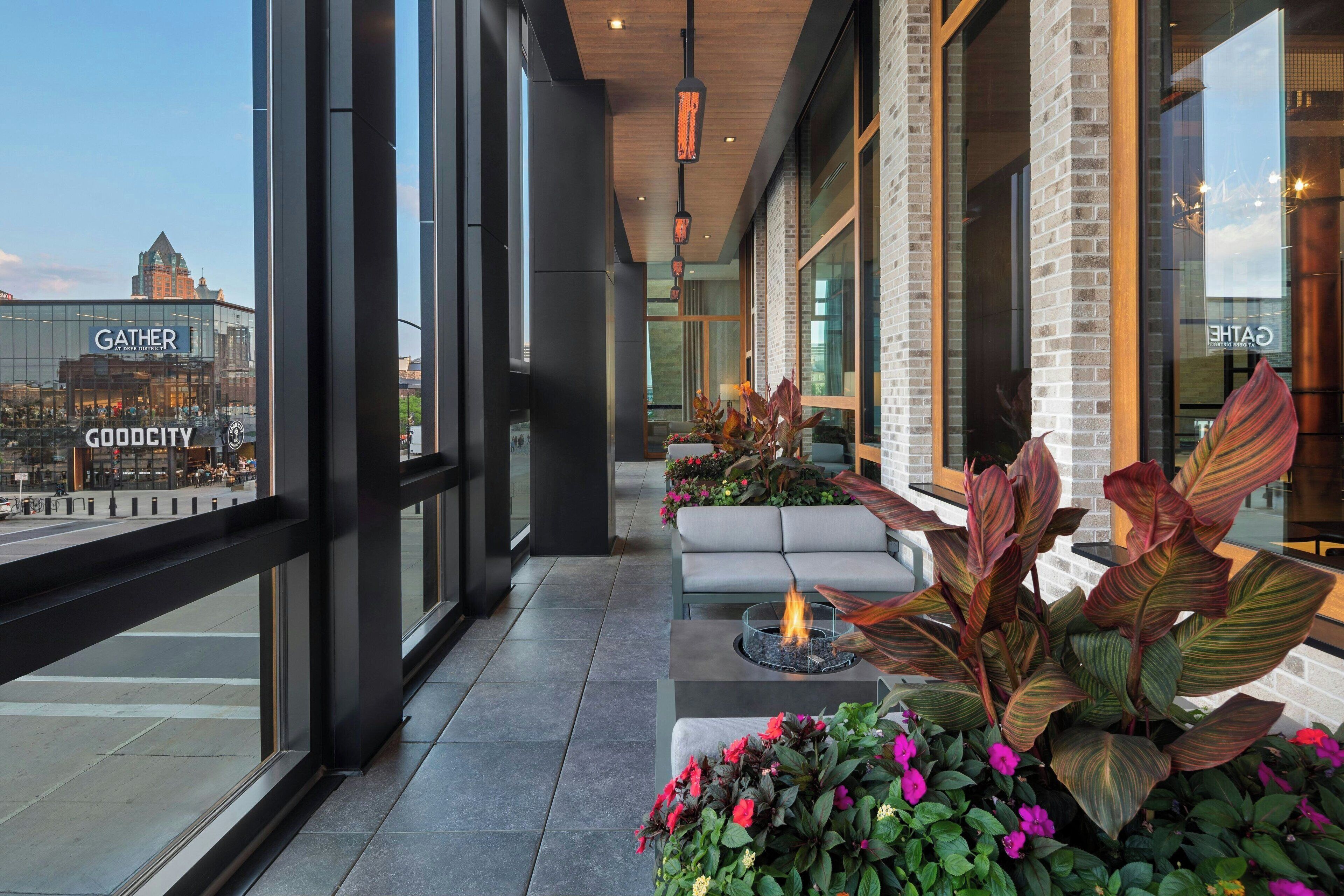 A modern indoor seating area with a fire feature, large windows, and a view of a cityscape including a 'GATHER' building.