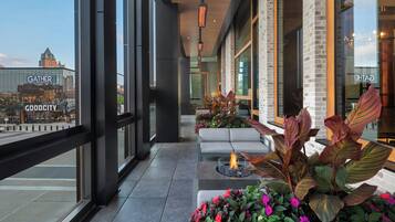 A modern indoor seating area with a fire feature, large windows, and a view of a cityscape including a 'GATHER' building.