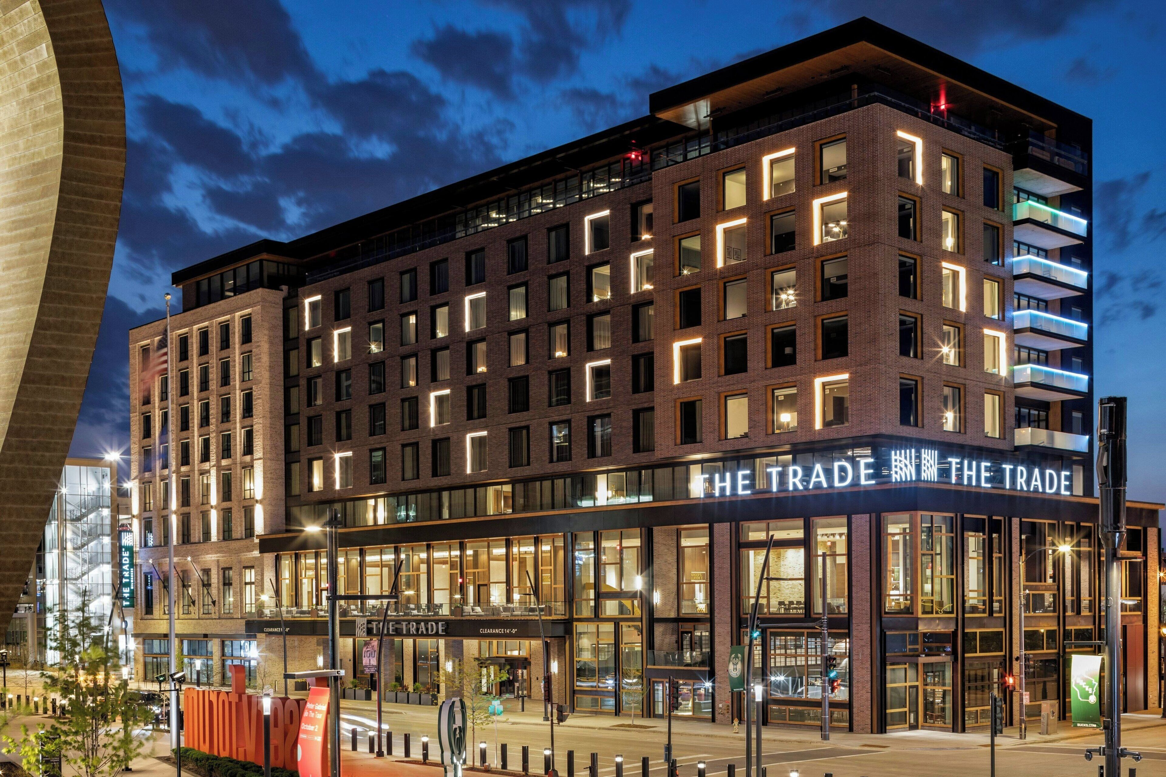 A modern hotel with multiple floors, large windows, and a prominent sign reading "THE TRADE".