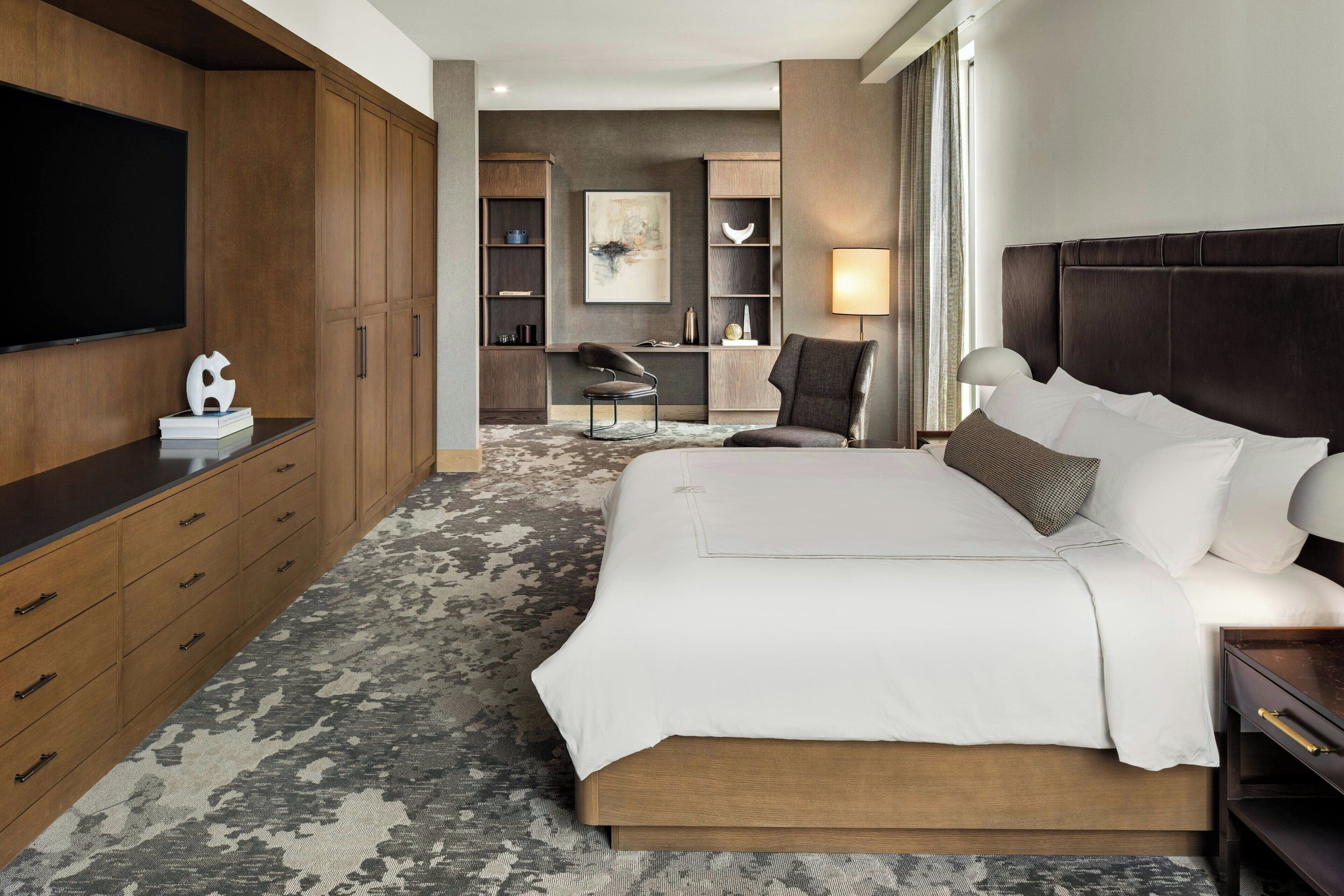 Une chambre d’hôtel avec un grand lit, une armoire en bois, un téléviseur à écran plat et un espace bureau avec une chaise.