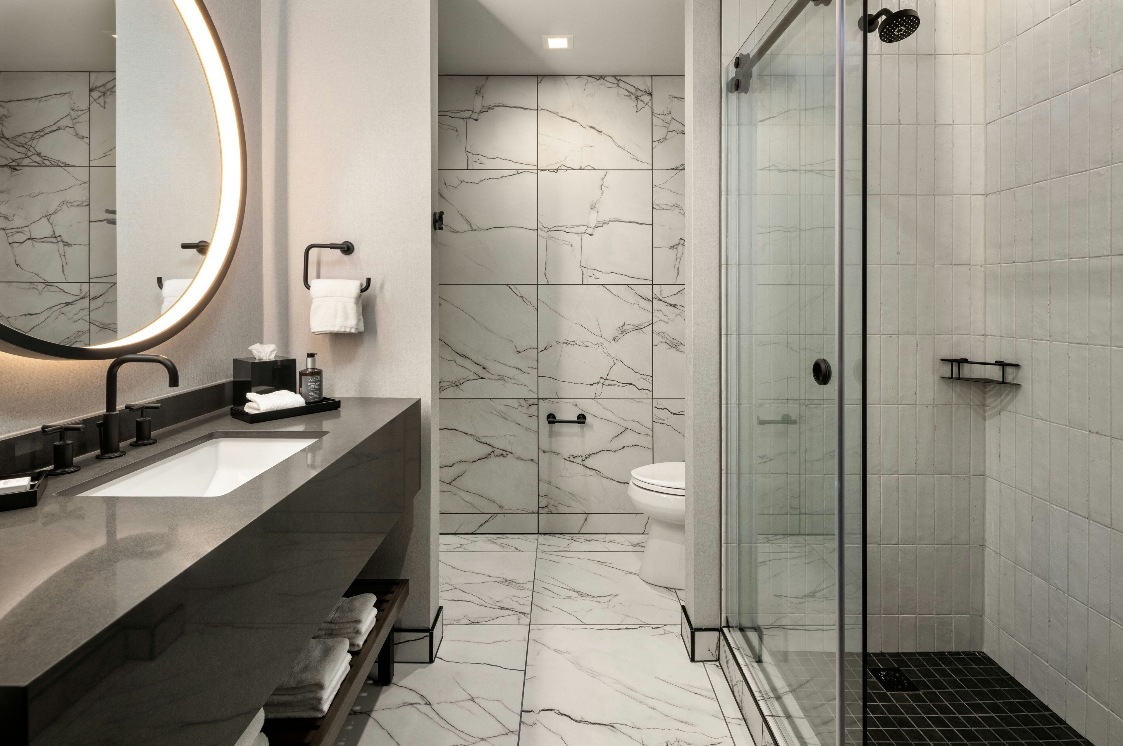A modern bathroom with a large mirror, two sinks, a toilet, and a glass-enclosed shower.