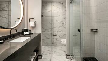 A modern bathroom with a large mirror, two sinks, a toilet, and a glass-enclosed shower.