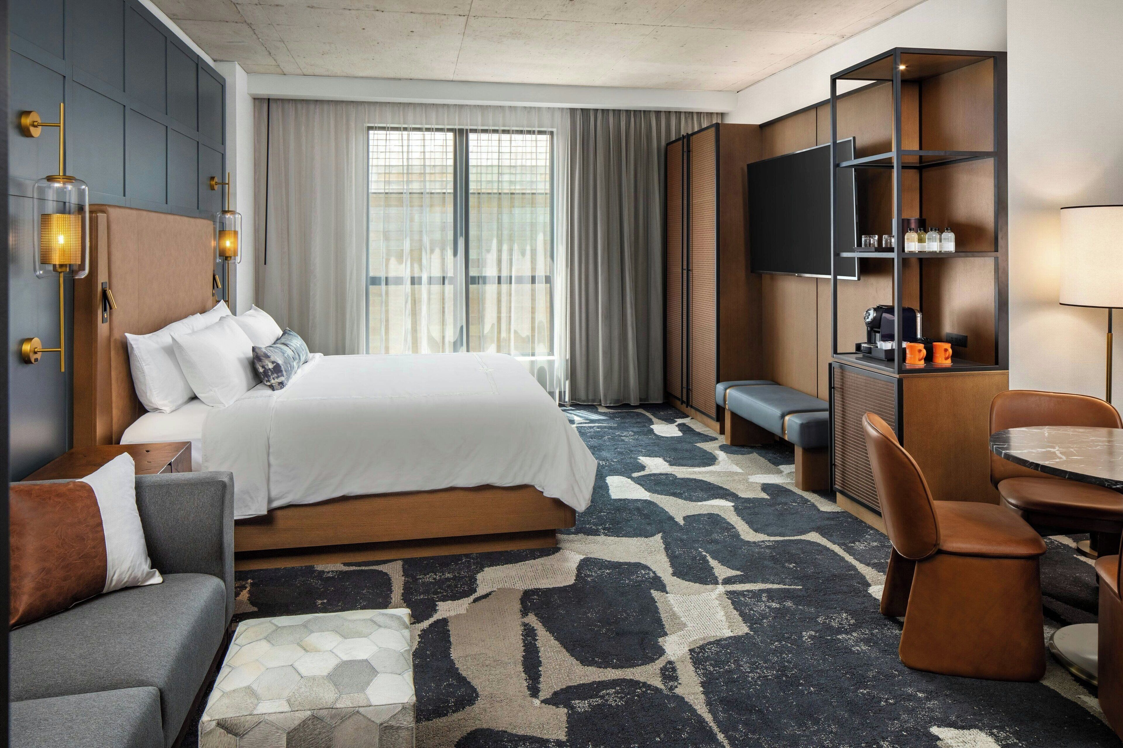 Una habitación de hotel con una cama grande, un sofá, un escritorio con una silla, un televisor y una estantería.