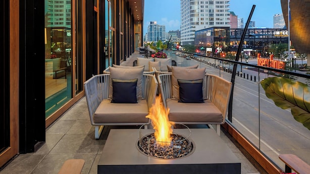 A modern outdoor seating area with a fire feature, overlooking a cityscape with tall buildings and a view of the street. - The Trade, Autograph Collection (Milwaukee)