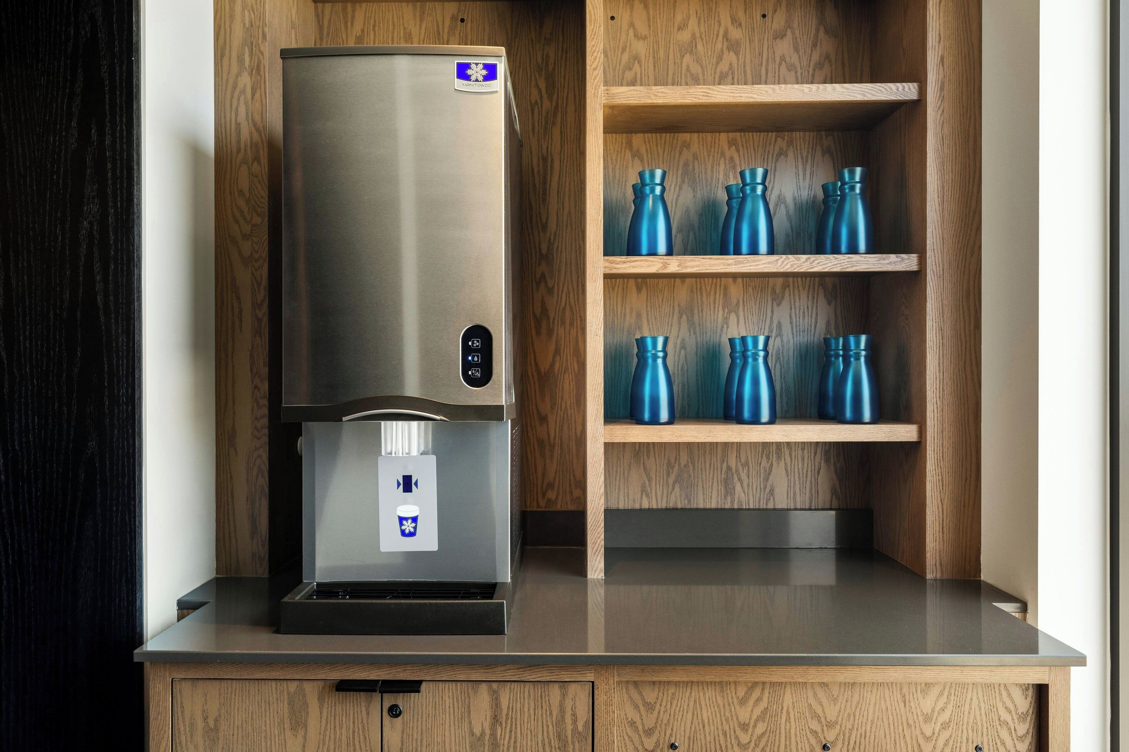 A stainless steel water dispenser with a control panel, a wooden cabinet with shelves, and a countertop.