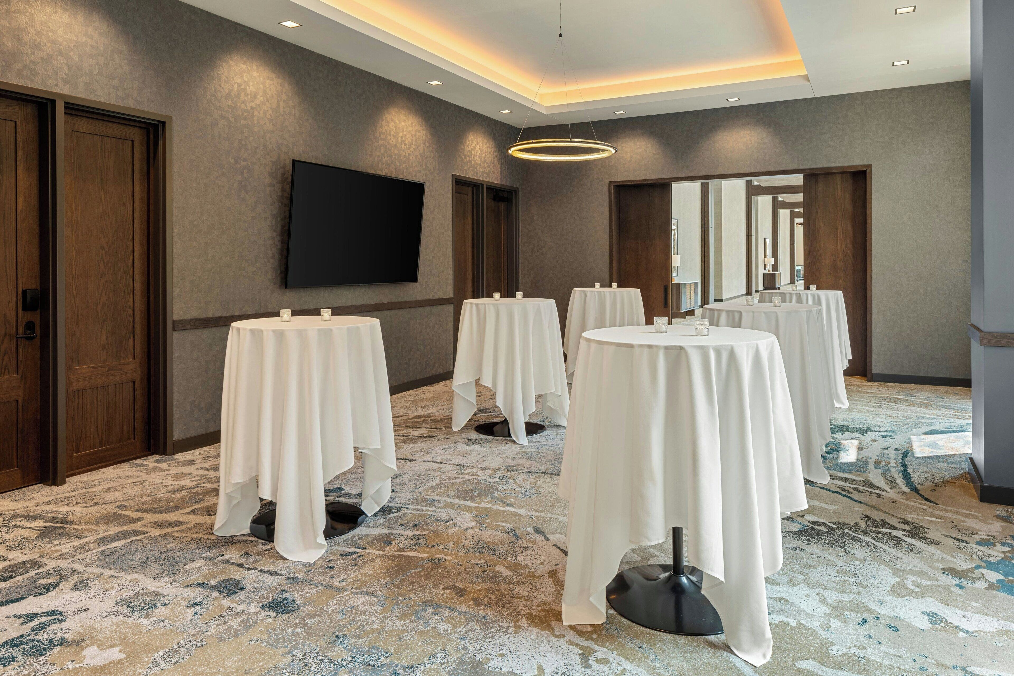 A conference room with multiple tables, a flat-screen TV, and a patterned carpet.