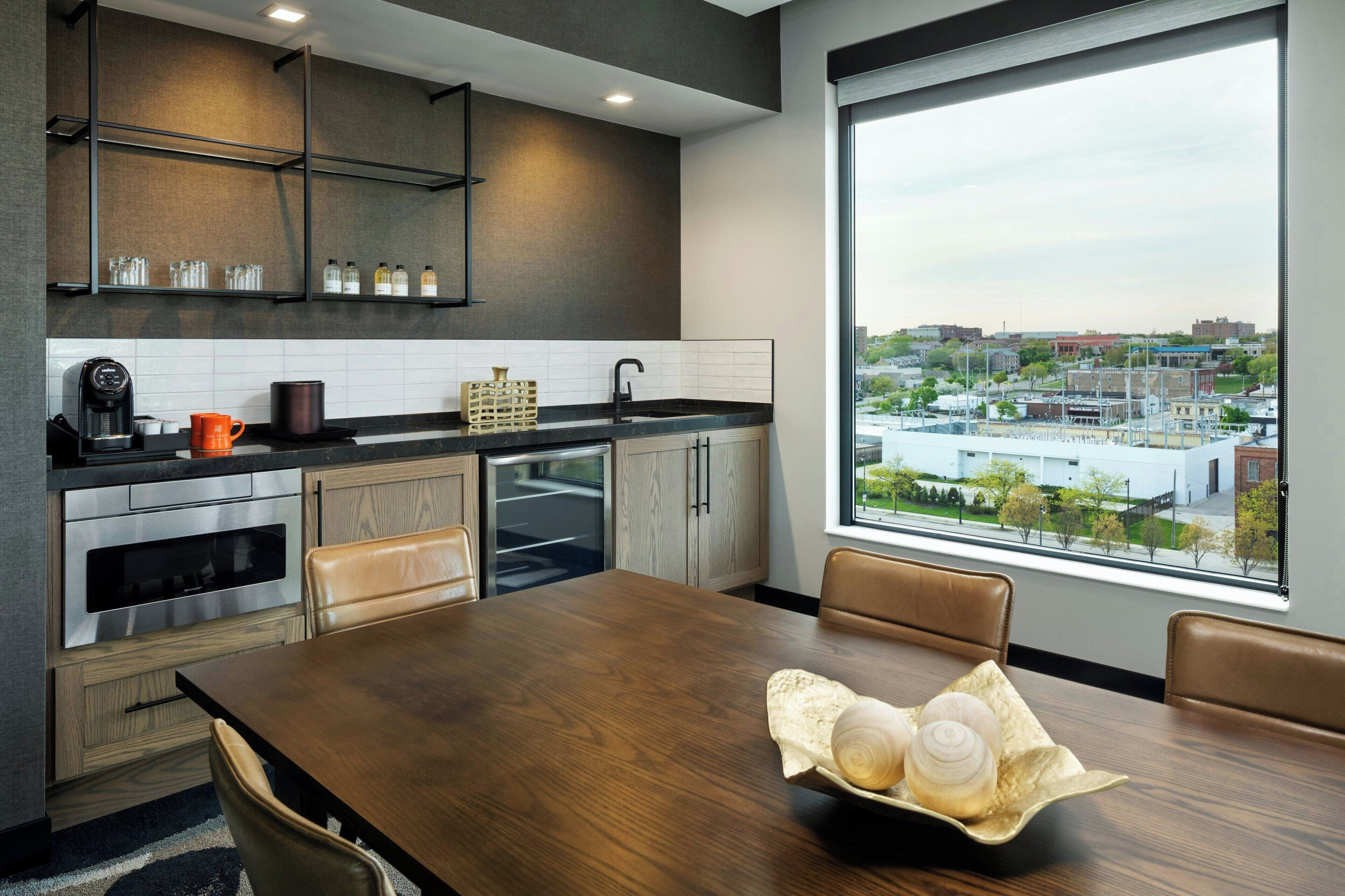 A modern kitchen with a large window, a dining table with chairs, and a view of the cityscape.