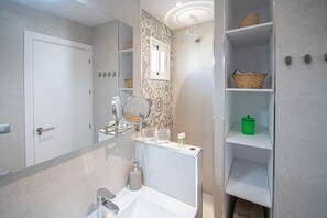 Ein modernes Badezimmer mit Waschbecken, Spiegel, Dusche und Regalen mit Körben und Pflegeprodukten.