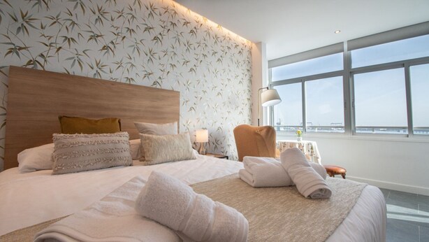 A hotel room with a large bed, a headboard, a view of the city, and a window. - Apartment La Atalaya de Cádiz (Cádiz)