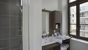 A modern bathroom with a shower, a sink with a mirror, and a window with a view of a building.