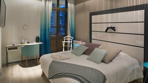 A modern hotel room with a bed, desk, chair, and a large window with curtains.