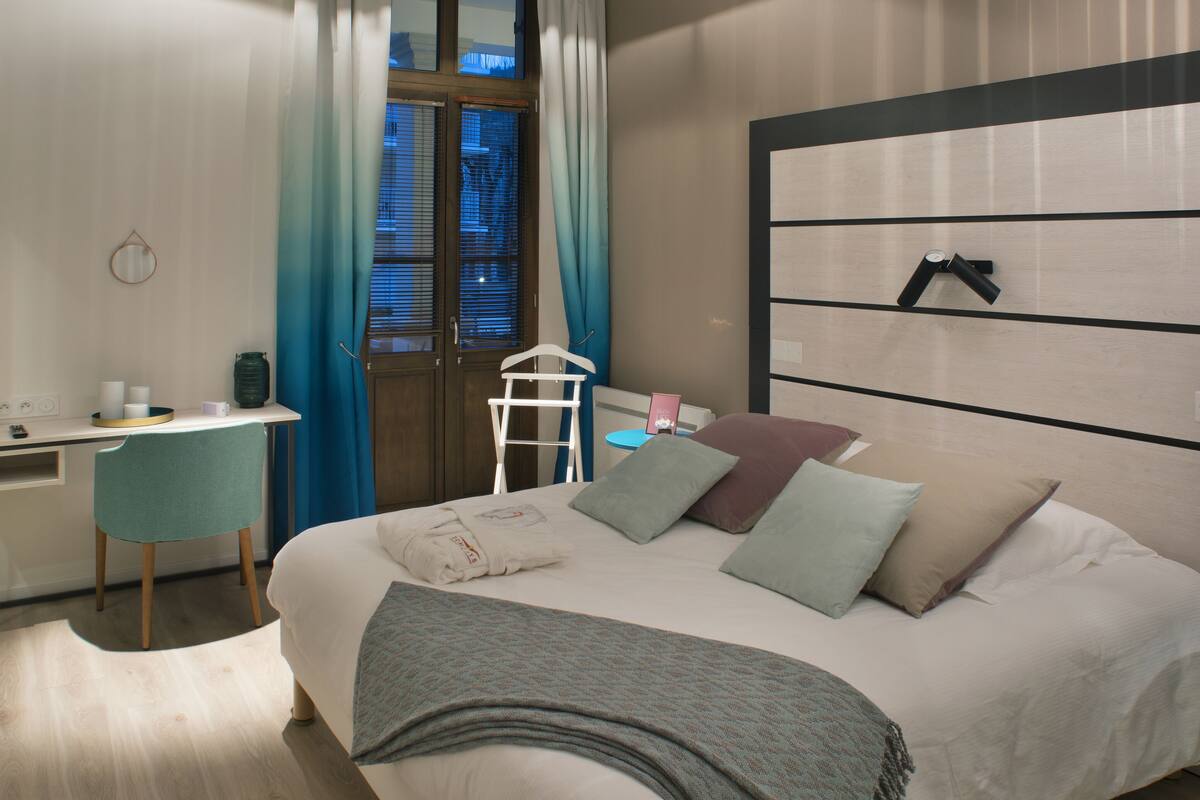 Une chambre d’hôtel moderne équipée d’un lit, d’un bureau, d’une chaise et d’une grande fenêtre avec des rideaux.