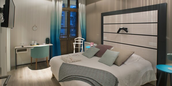 A modern hotel room with a bed, desk, chair, and a large window with curtains.
