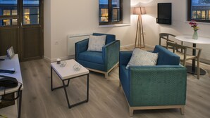 A modern living room with a desk, two blue armchairs, a small table, and a lamp.