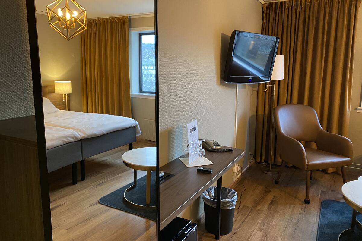 Una habitació d'hotel amb llit, escriptori amb cadira, televisió i finestra amb cortines.