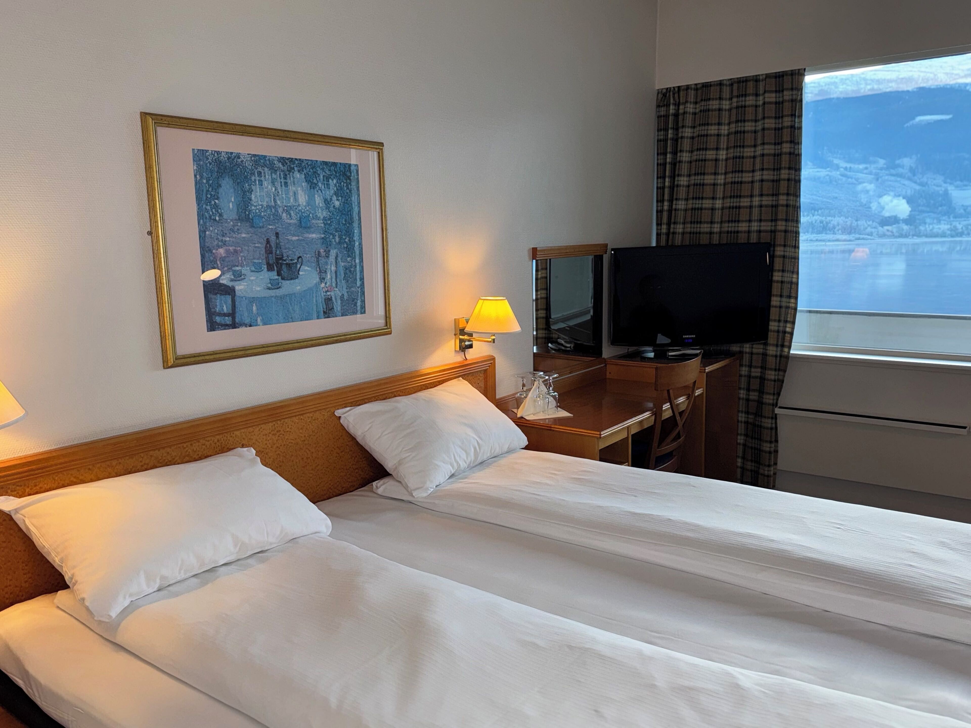 Une chambre d’hôtel avec deux lits, une télévision, un bureau avec une lampe et un tableau au mur.