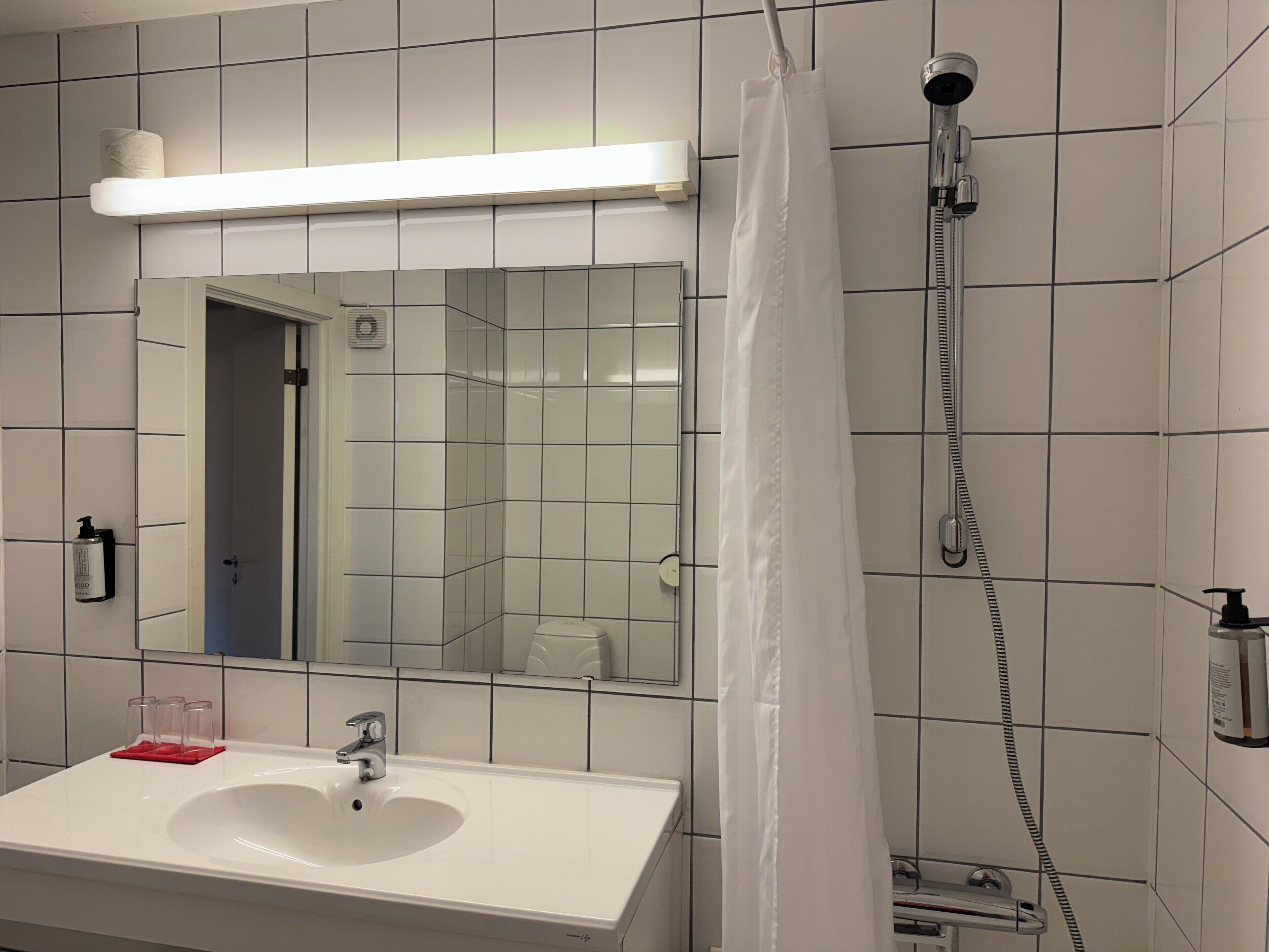 A bathroom with a white sink, mirror, and shower.