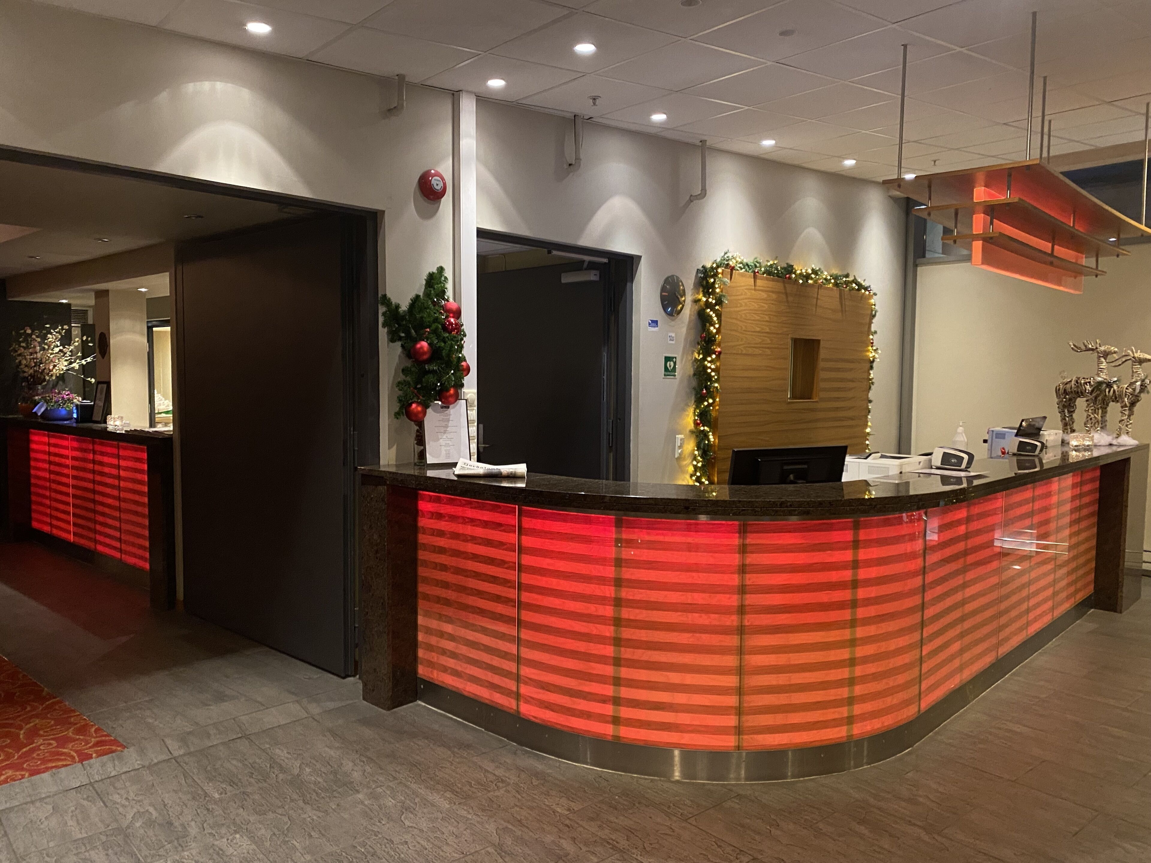 A hotel reception area with a red and black striped reception desk, a Christmas tree, and a clock on the wall.