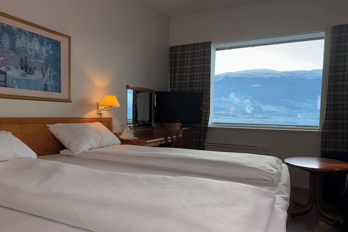 Habitació d'hotel amb dos llits, escriptori amb cadira, televisió i finestra amb vista a un paisatge nevós.