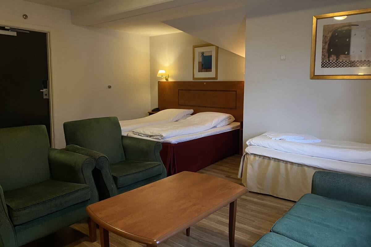 Habitació d'hotel amb dos llits individuals, una taula de fusta, dues butaques verdes, un petit escriptori de fusta i un quadre encapçalat al mur.
