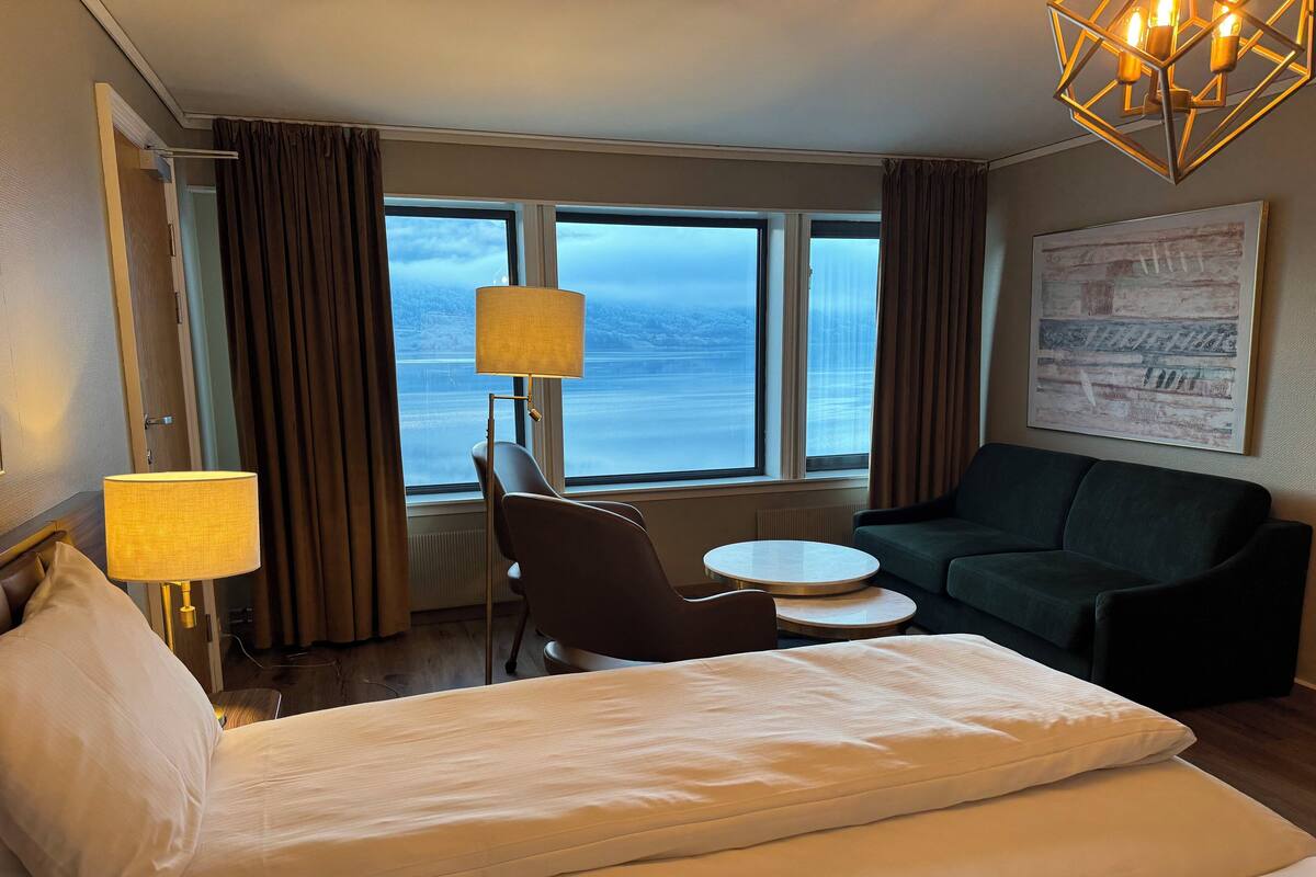 Habitació d'hotel amb llit, cadira, sofà, taula i una finestra gran que dona al mar.