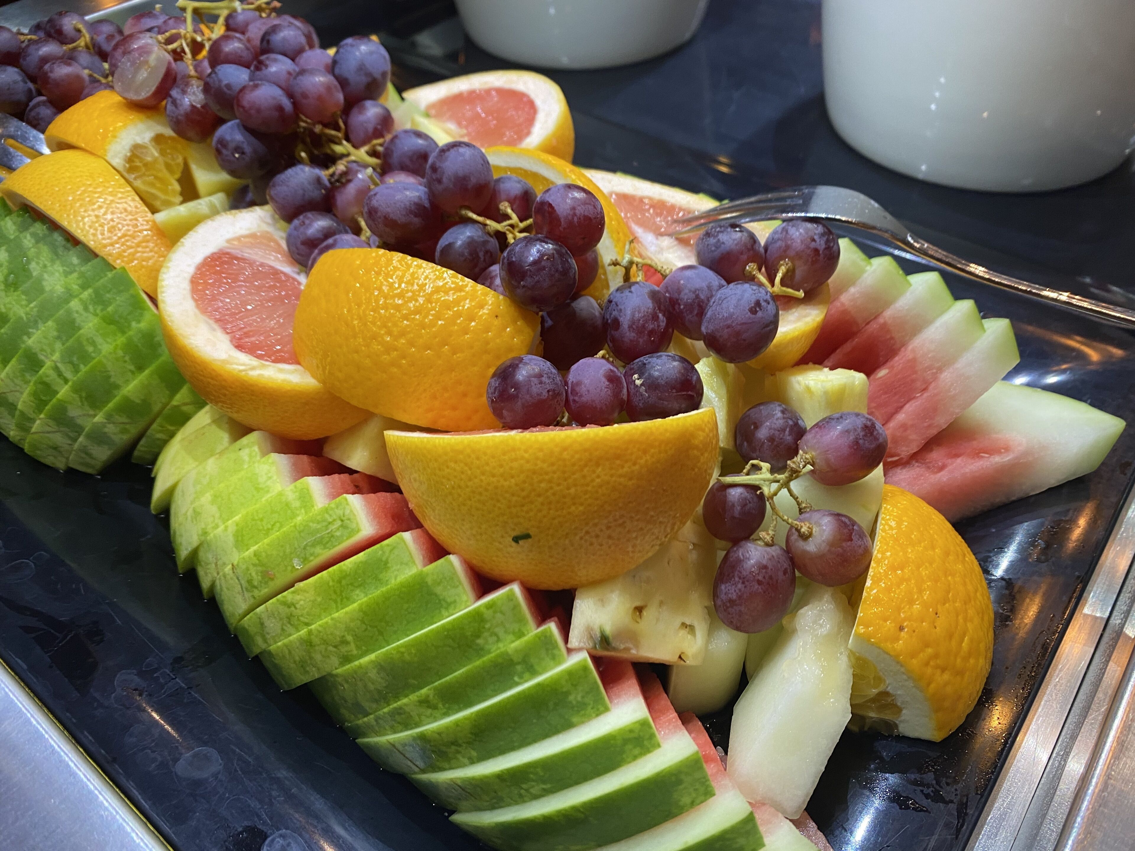 Una bandeja con frutas cortadas, como naranjas, uvas y sandía.
