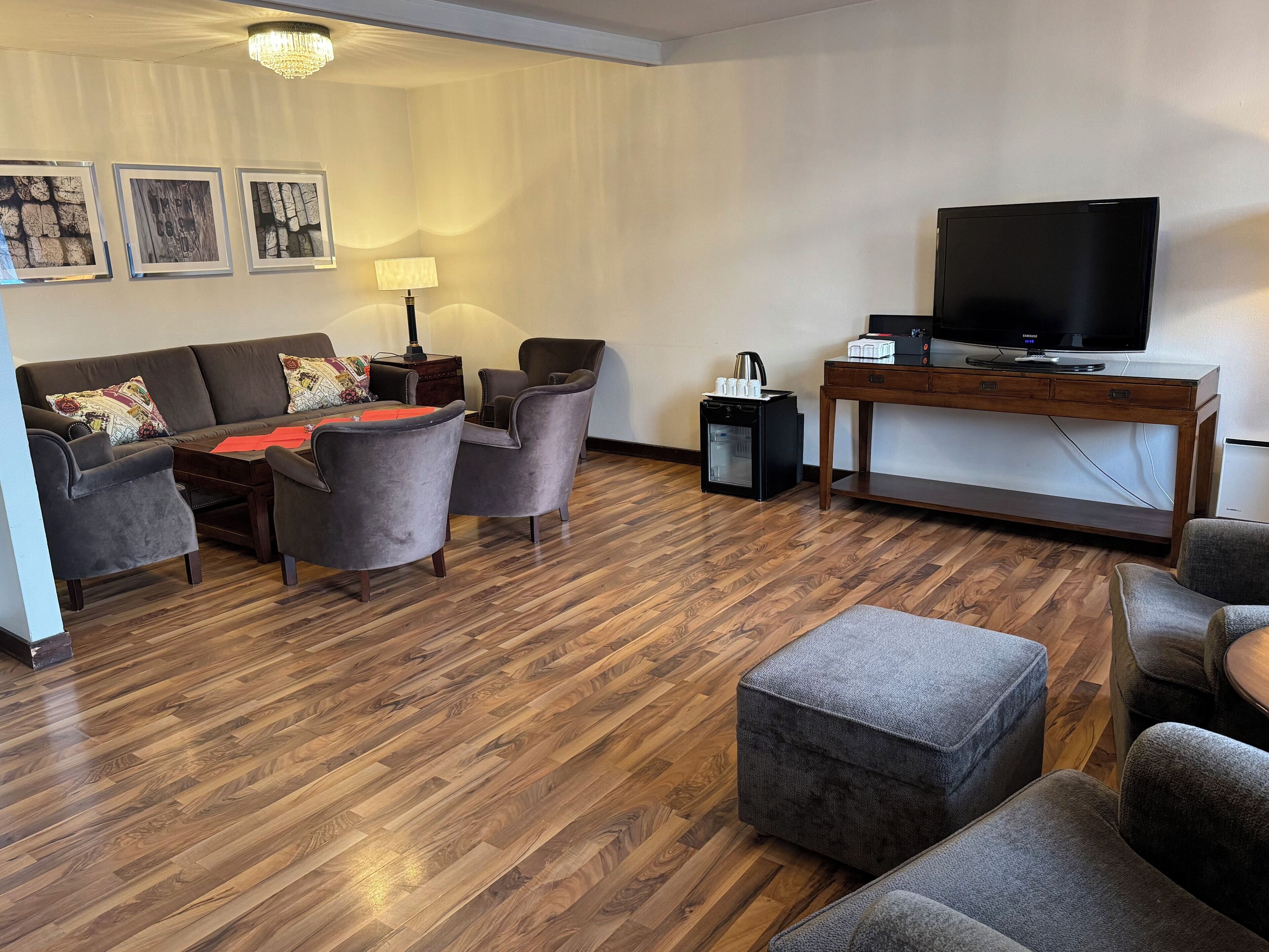 Uma sala de estar moderna com sofá, poltronas, mesa de centro, televisão e um frigorífico pequeno.